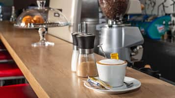A coffee bar with a coffee machine, sugar and salt shakers, and a cup of coffee on a saucer.