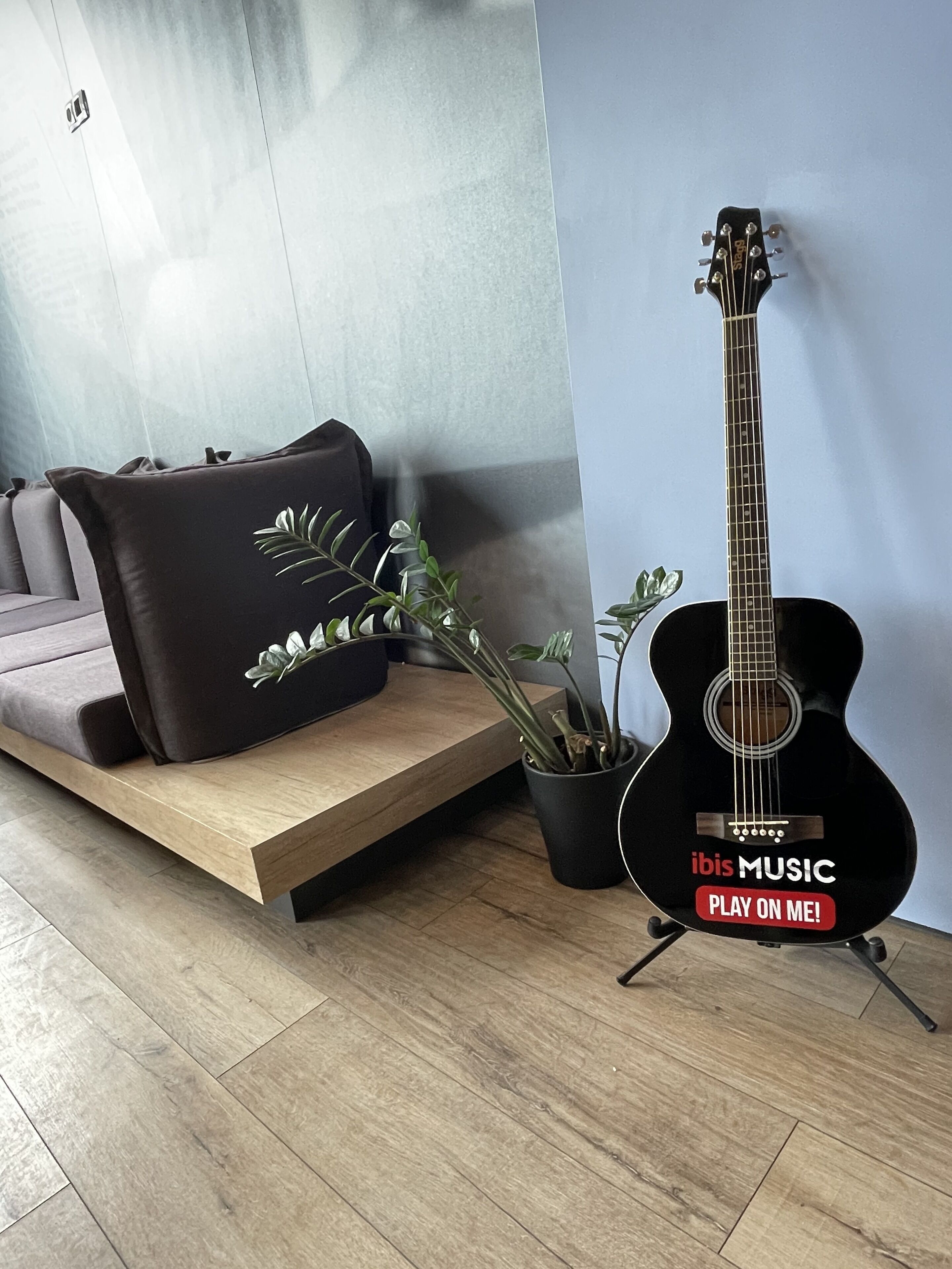 A modern living room with a wooden bench, a black guitar, and a potted plant.