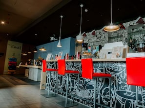A bar area with red bar stools, hanging pendant lights, and a wall with black and white graffiti-style artwork.