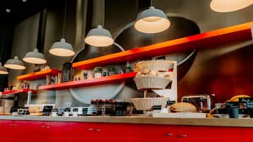 A modern café interior with red cabinetry, multiple hanging pendant lights, and shelves displaying various baked goods and coffee items.