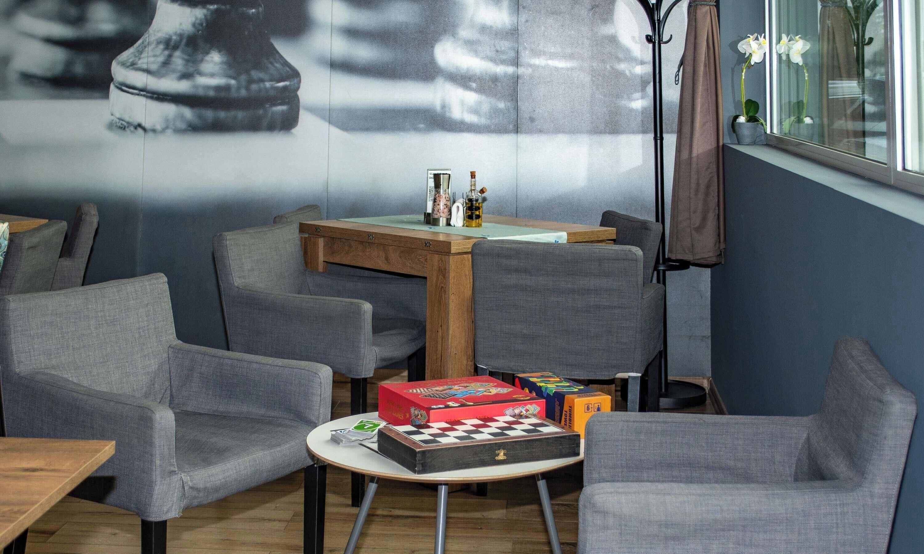 Una habitación con sillas tapizadas en gris, una mesa de madera con un tablero de ajedrez y una pared con un mural grande.
