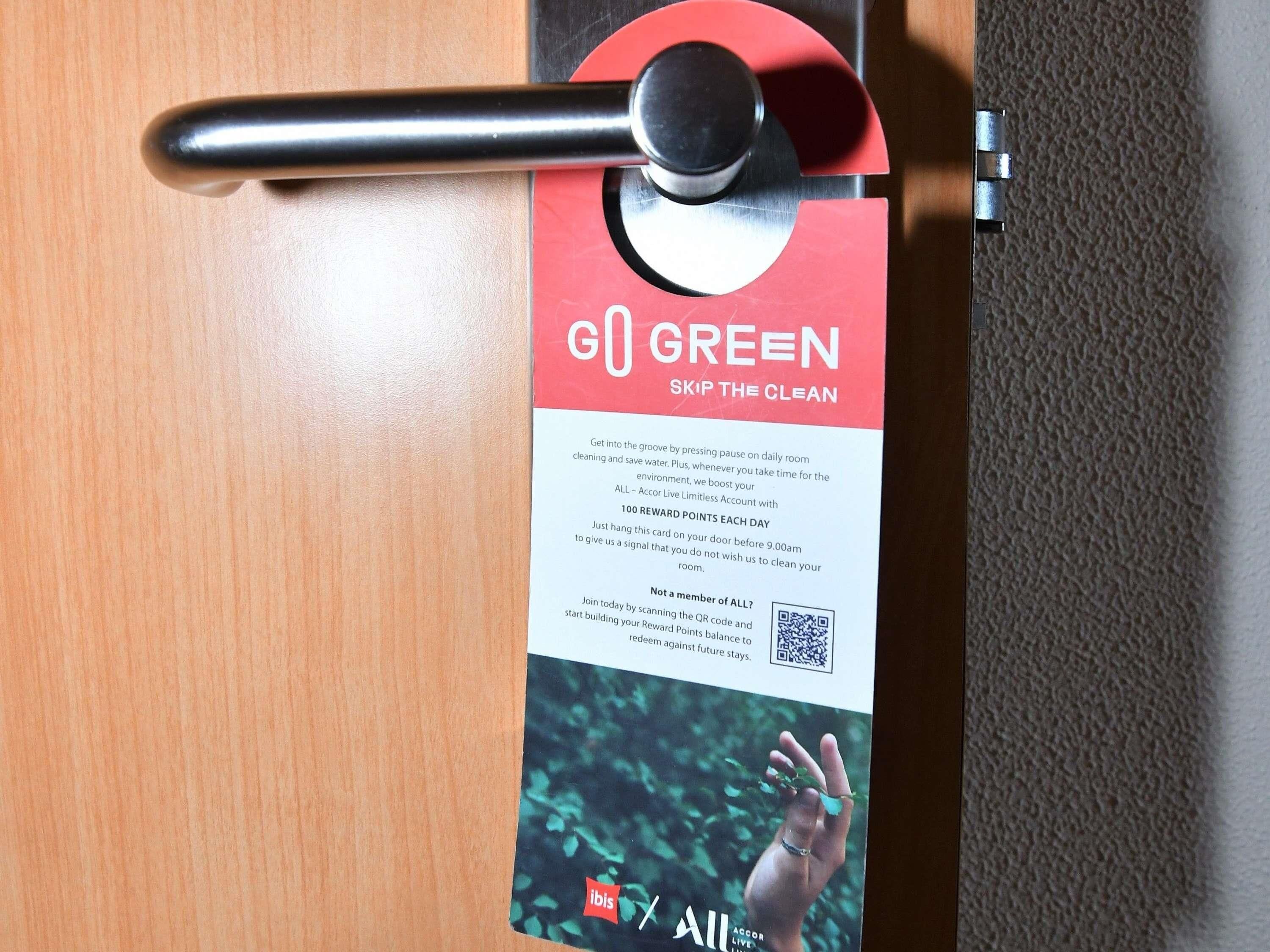 Una puerta con un atril para tarjetas que muestra un letrero 'GO GREEN', un código QR y un mensaje sobre un programa de recompensas.