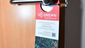 Una puerta con un atril para tarjetas que muestra un letrero 'GO GREEN', un código QR y un mensaje sobre un programa de recompensas.