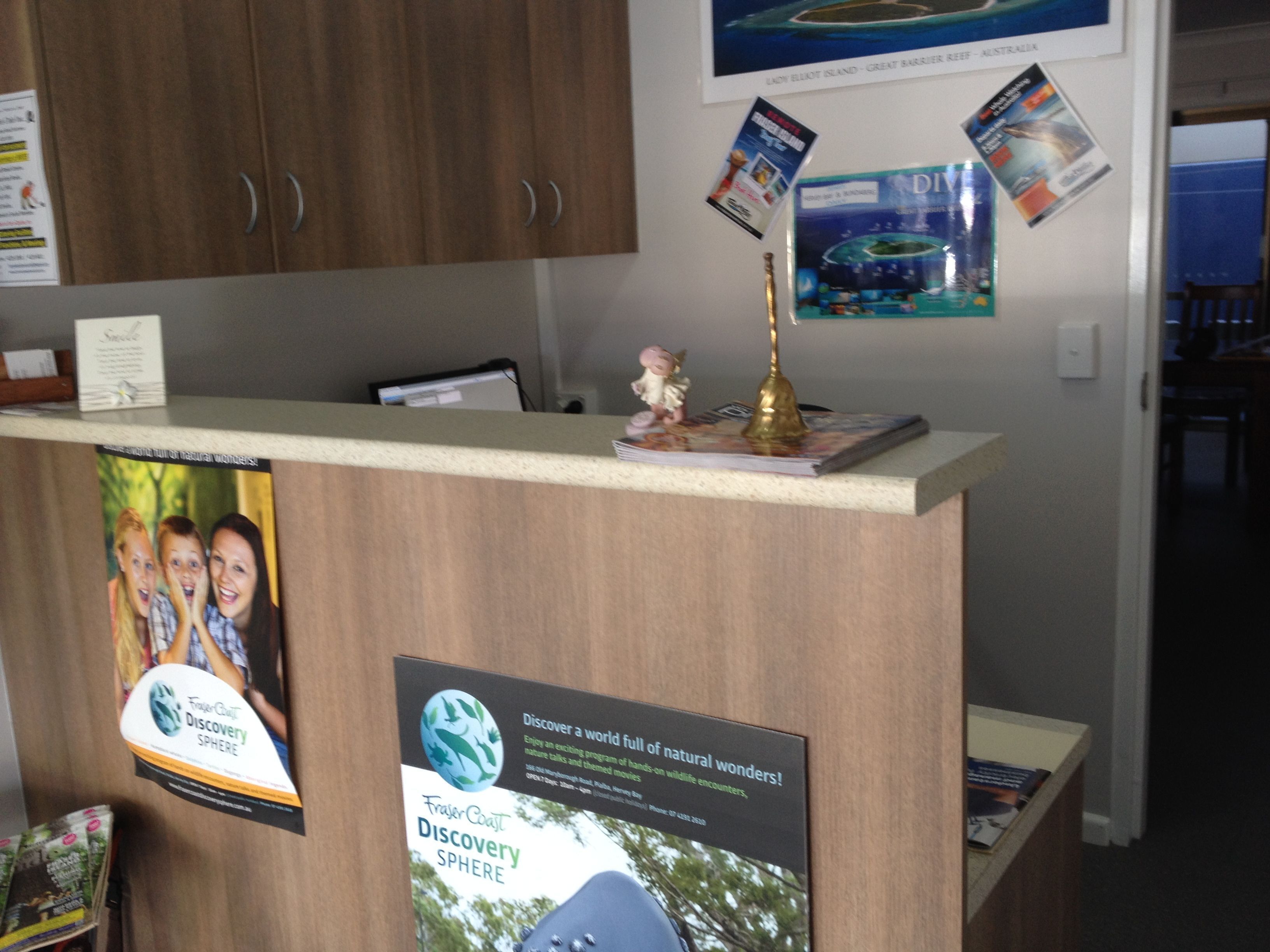Un comptoir d’accueil avec un revêtement en bois, une petite statue et plusieurs affiches d’information.