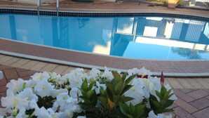 Uma piscina com borda azulejada e um canteiro de flores com flores brancas e vermelhas em primeiro plano.