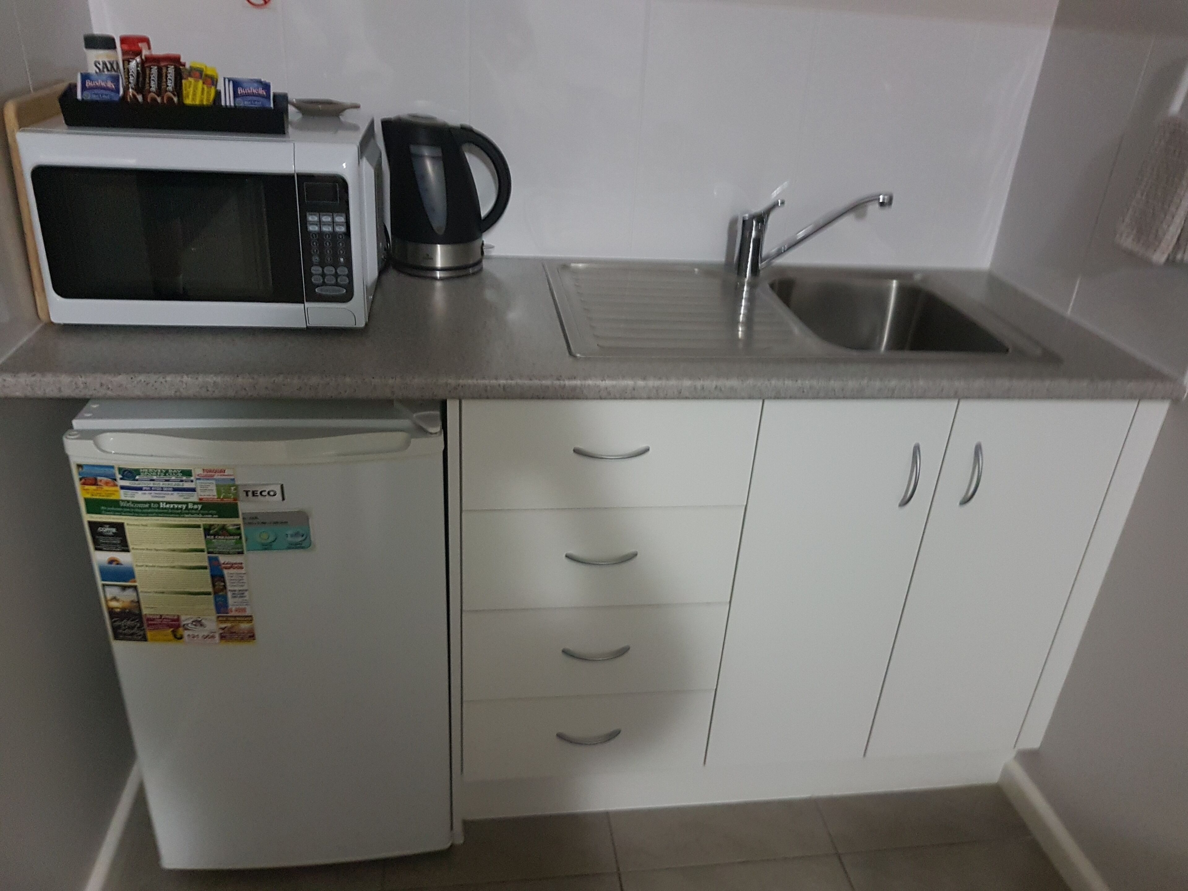 Una cucina compatta con forno a microonde, macchina del caffè e frigorifero.