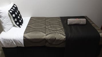 A single bed with a patterned bedspread, a black and white pillow, and a folded towel on the side.