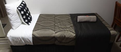 Una cama individual con una colcha estampada, una almohada blanco y negro y una toalla doblada al lado.