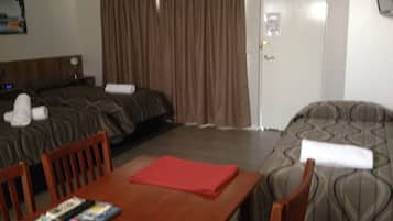 A hotel room with two beds, a wooden table with magazines, and a door with a light switch.