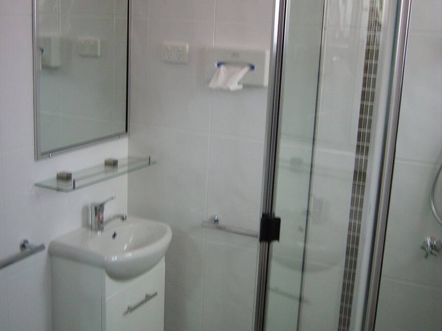 A bathroom with a glass shower enclosure, a sink, and a mirror.