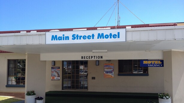 O Motel Main Street com uma área de recepção, um aviso indicando quarto disponível e plantas em vasos.