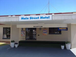 The Main Street Motel with a reception area, a sign indicating a motel vacancy, and potted plants. - Main Street Motel (Pialba)