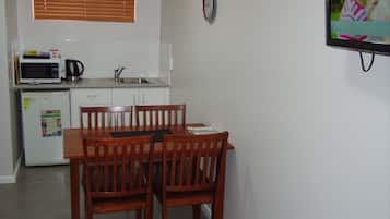 Eine kompakte Küche mit Mikrowelle, Wasserkocher und Kühlschrank. Ein Esstisch mit Stühlen und eine Uhr sind an der Wand angebracht.