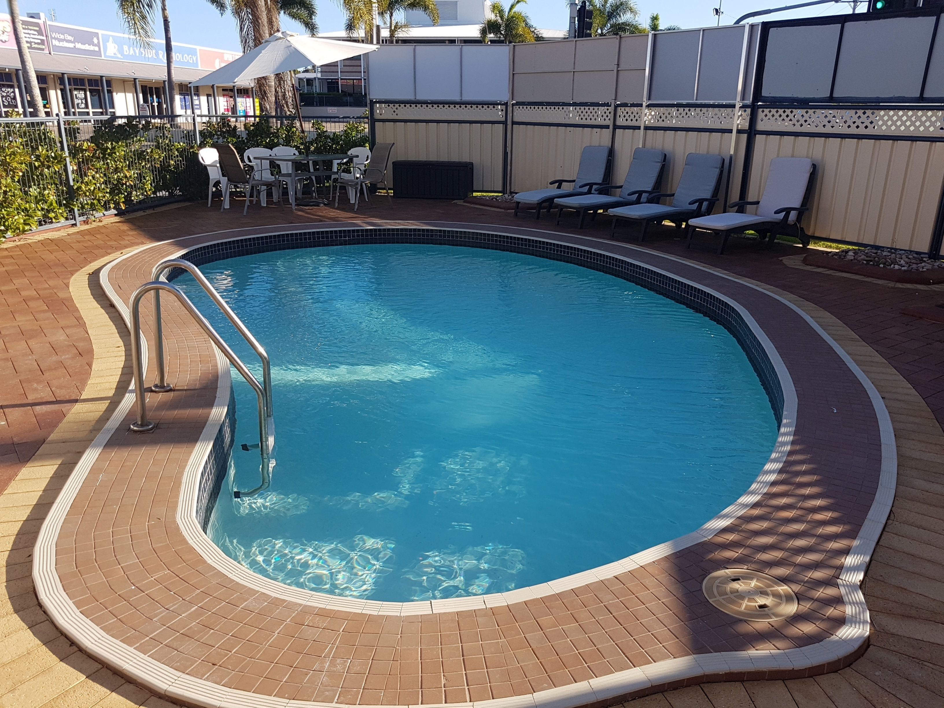 Une piscine avec une terrasse carrelée, des chaises longues et une table avec des parasols.