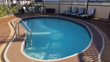 A swimming pool with a tiled deck, lounge chairs, and a table with umbrellas.