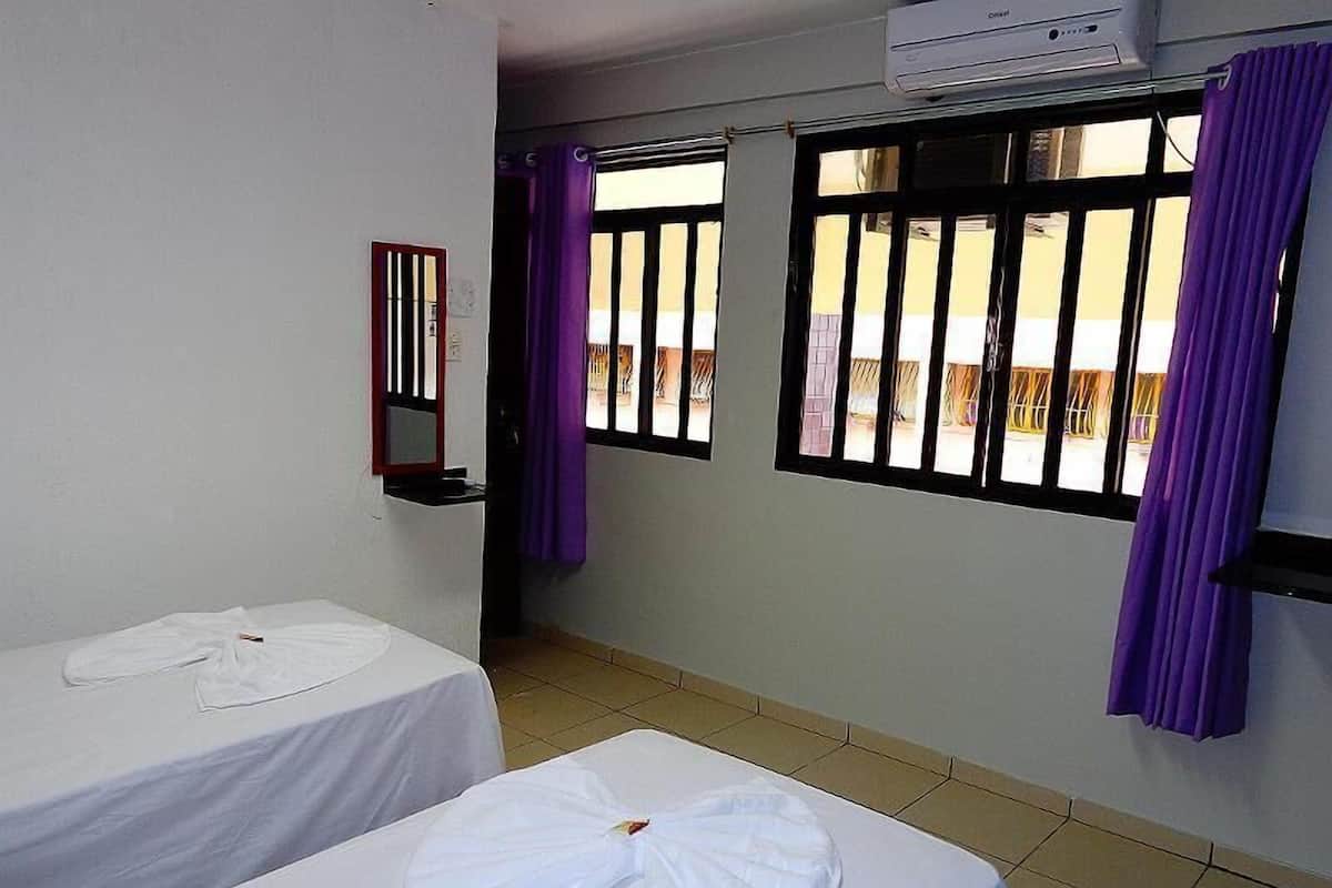A hotel room with two beds, a window with bars, a mirror, and purple curtains.