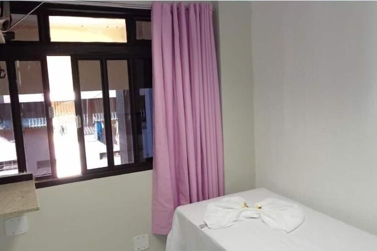 A small, single-bed room with a window and a curtain.