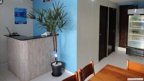 A reception area with a wooden counter, a potted plant, a blue wall, a refrigerator, and a dining table with chairs. - Pousada Damasco (Brasília)