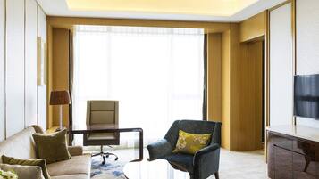 A modern hotel room with a sofa, armchair, coffee table, desk, and TV.