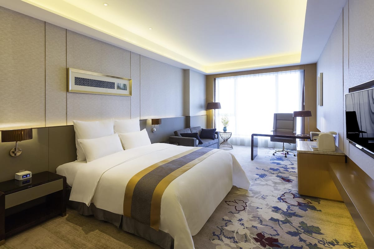 A hotel room with a large bed, a desk, a chair, a TV, and a window.