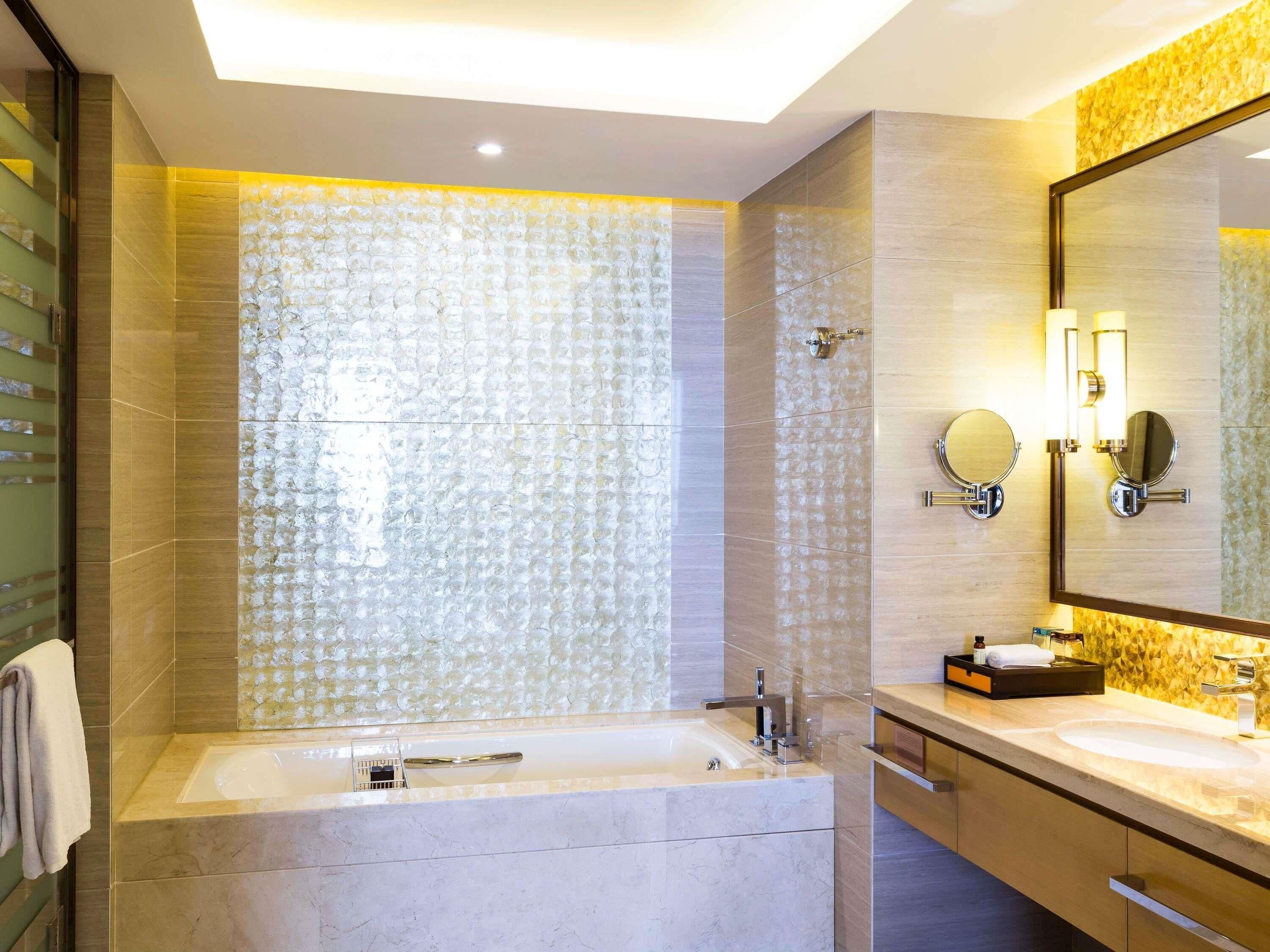 A modern bathroom with a large bathtub, two sinks, and a mirror with lights.