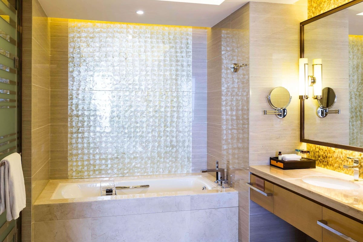 A modern bathroom with a large bathtub, two sinks, and a mirror with lights.