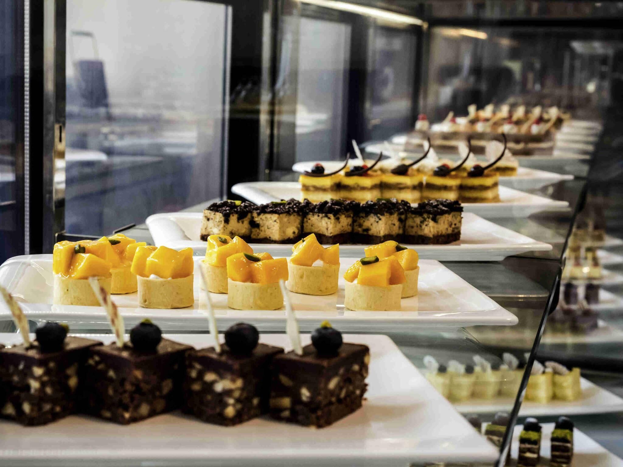 A display of various desserts in a glass case, including mango-topped treats and chocolate squares.
