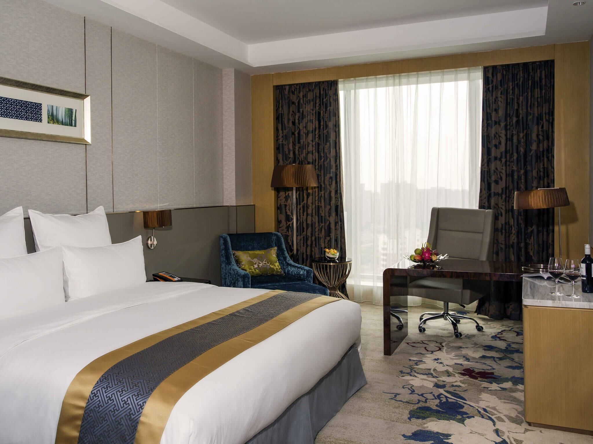A hotel room with a large bed, a desk, a chair, a lamp, and a window with curtains.