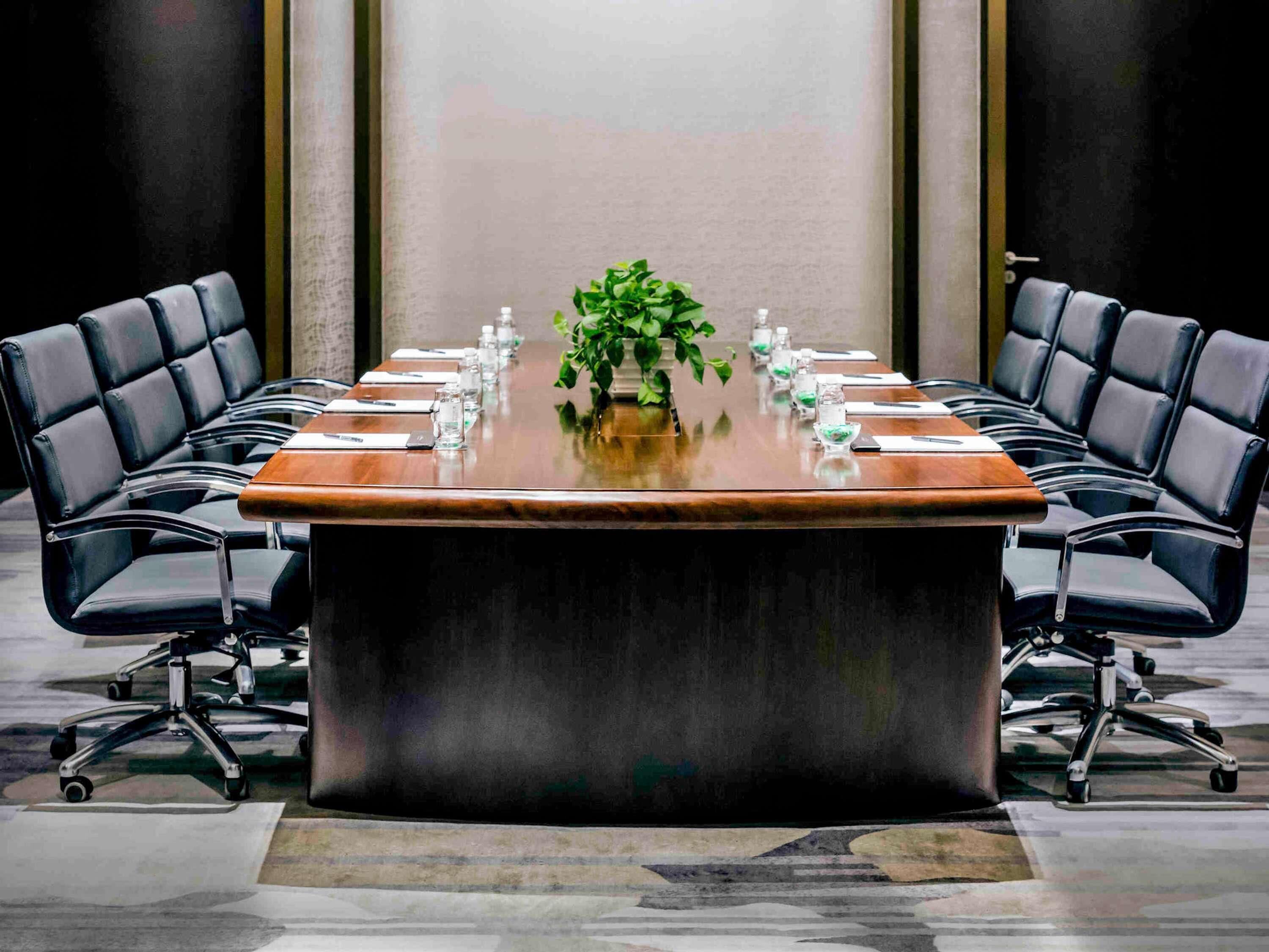 A conference room with a long table, black leather chairs, a potted plant, and water bottles.