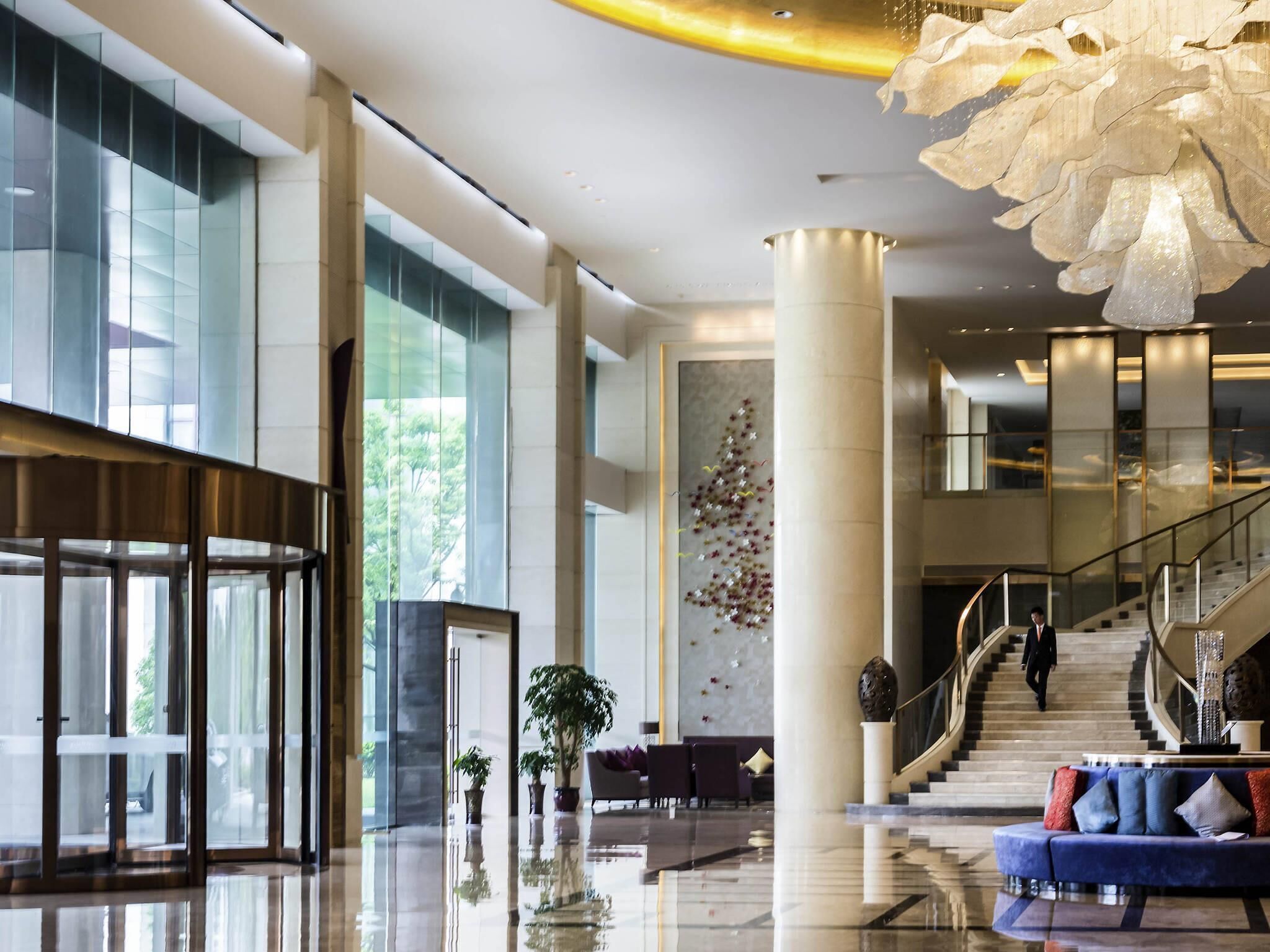 A spacious lobby with a grand staircase, a reception desk, and a large chandelier.