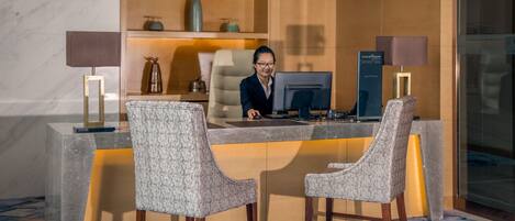 Un mostrador de recepción con una computadora, dos sillones tapizados y un suelo de mármol.