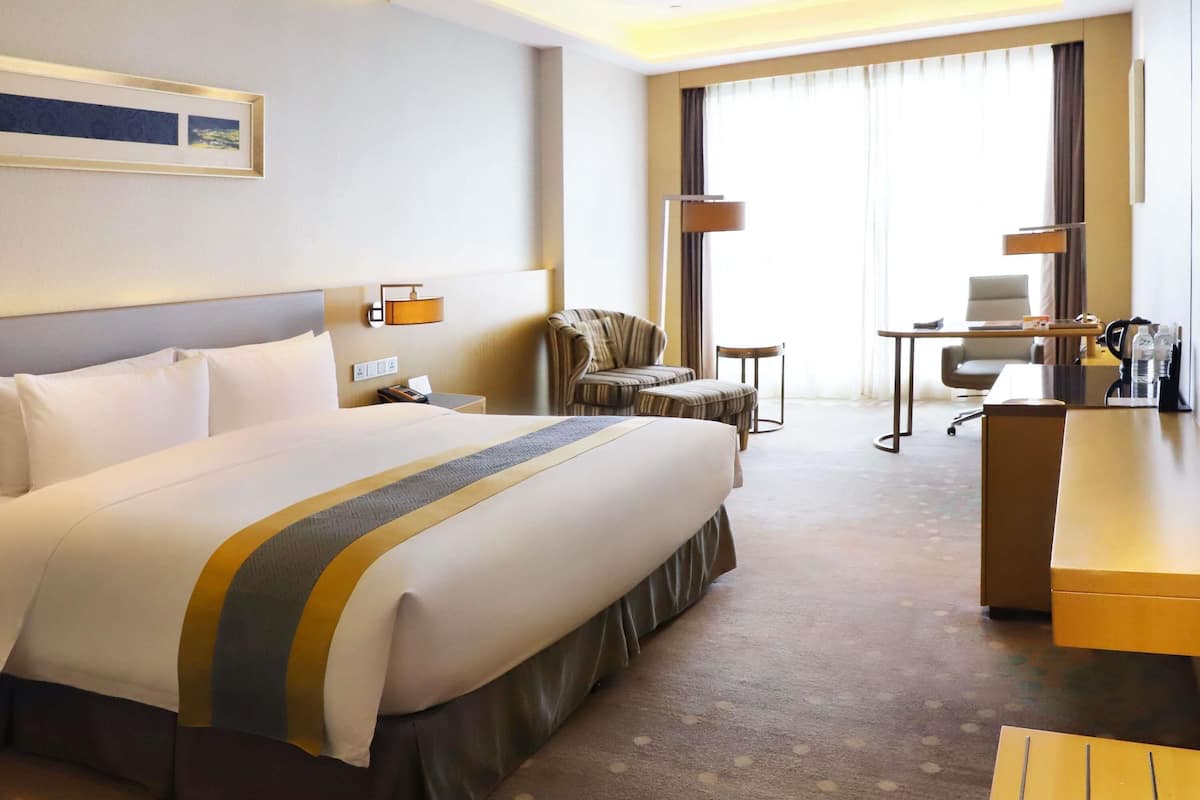 A hotel room with a large bed, a desk, a chair, and a sofa.