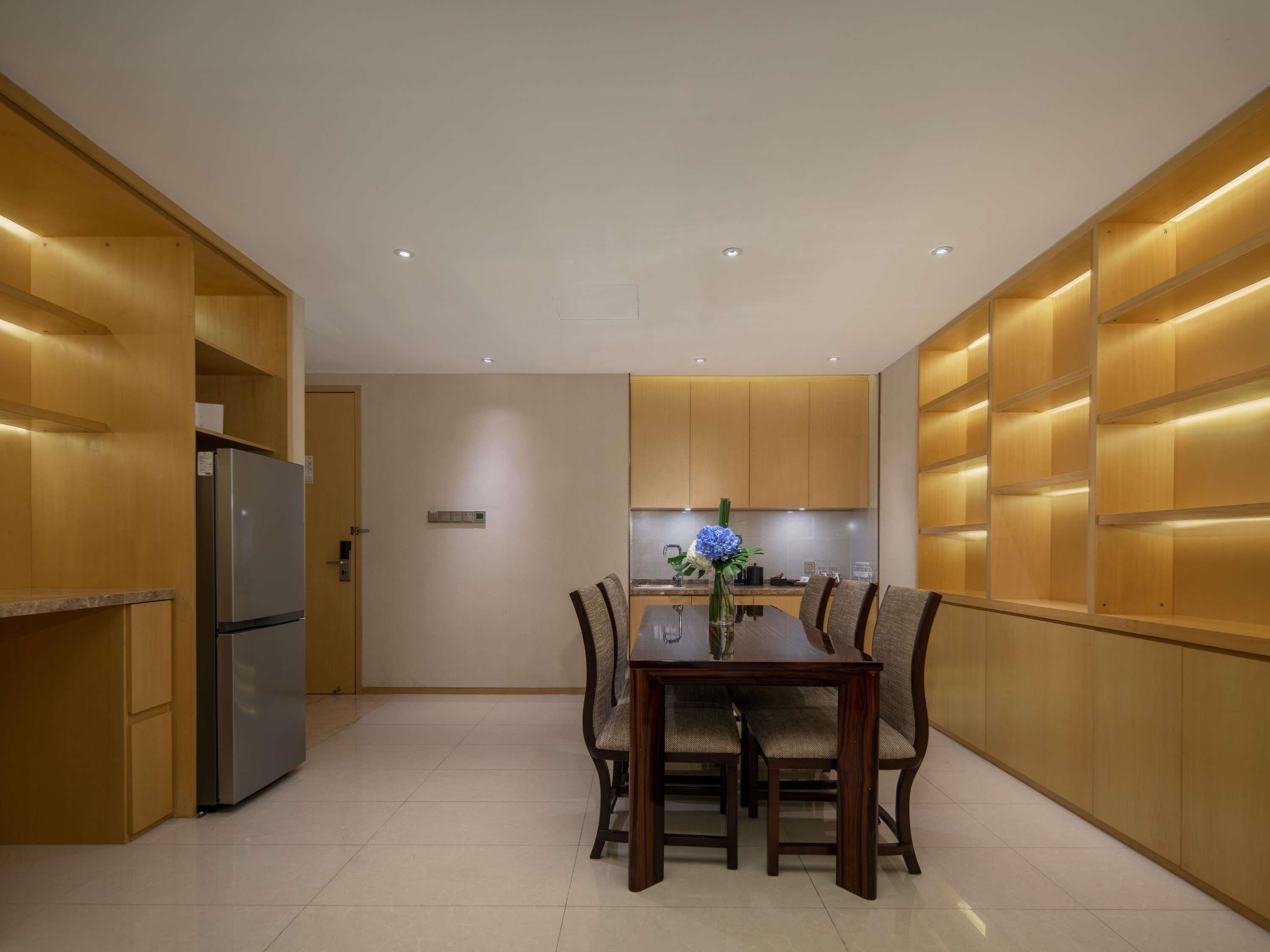 A modern kitchen with built-in wooden cabinets, a stainless steel refrigerator, and a dining table with chairs.