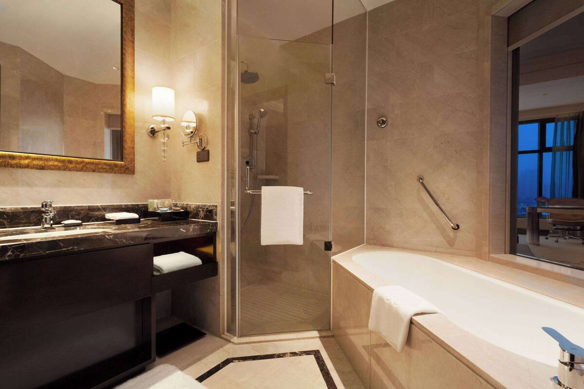 A modern bathroom with a glass-enclosed shower, a large bathtub, and a vanity with a mirror and two sinks.