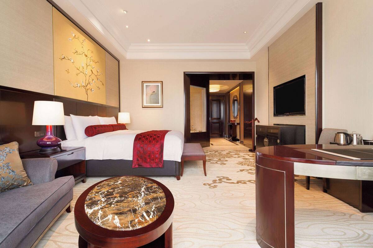 A hotel room with a bed, a sofa, a coffee table, a TV, and a desk.