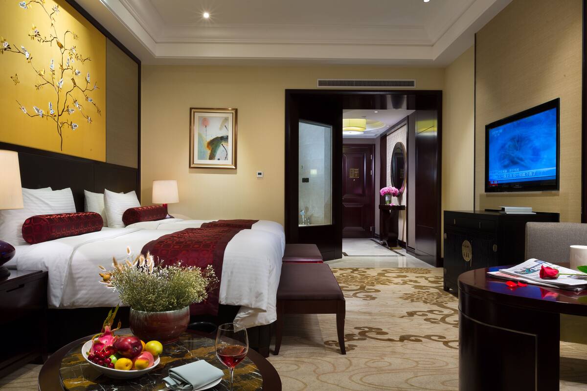 A hotel room with a bed, bedside table, TV, and a dining area with a table and chairs.
