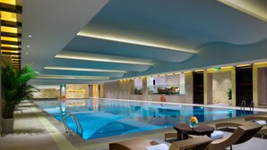 An indoor swimming pool with lounge chairs and a table, surrounded by walls with a modern design and a ceiling with recessed lighting. - Wyndham Grand Xian South (Xi'an)