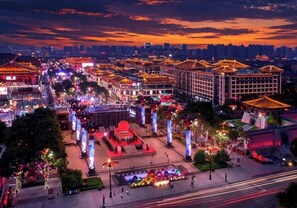 A cityscape at dusk with illuminated buildings, a central plaza with a fountain, and a modern high-rise in the background. - Wyndham Grand Xian South (Xi'an)
