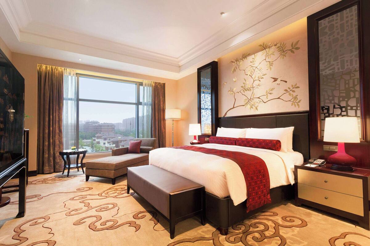 A hotel room with a large bed, a desk, a chair, a sofa, and a view of the city.