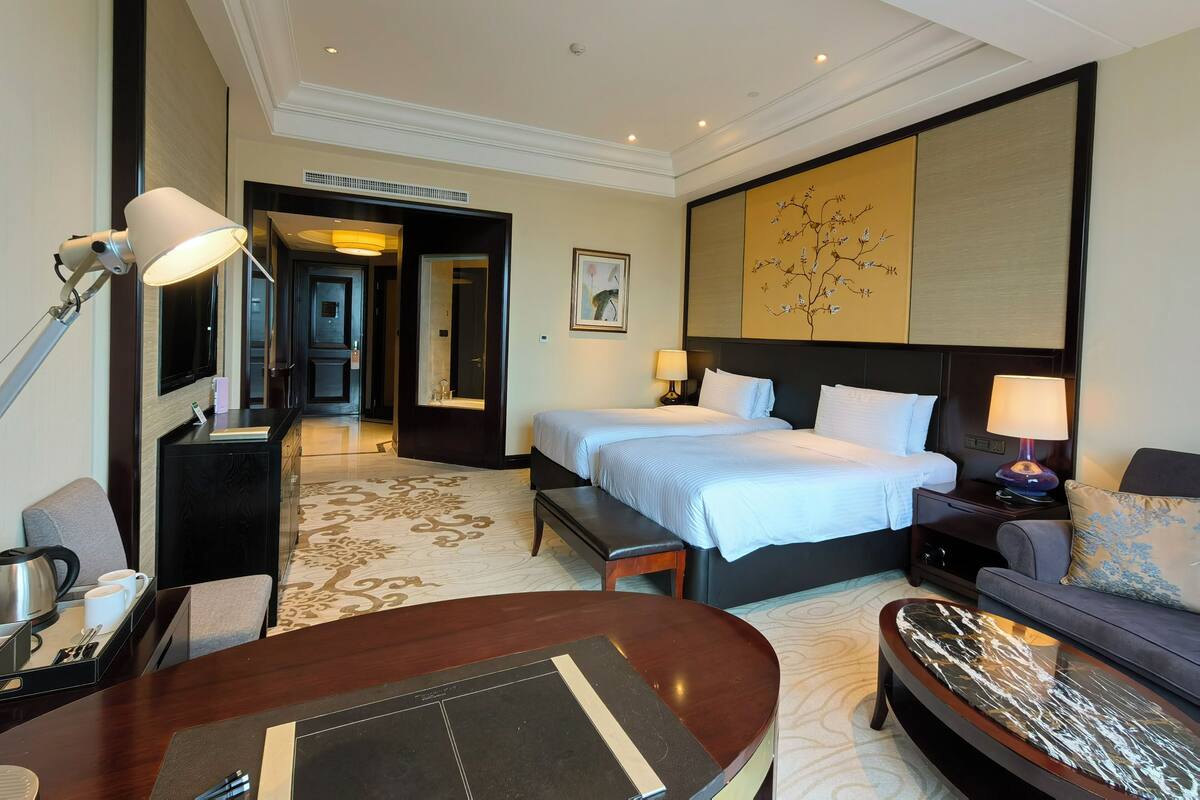 A hotel room with two beds, a sofa, a dining table, and a large artwork on the wall.