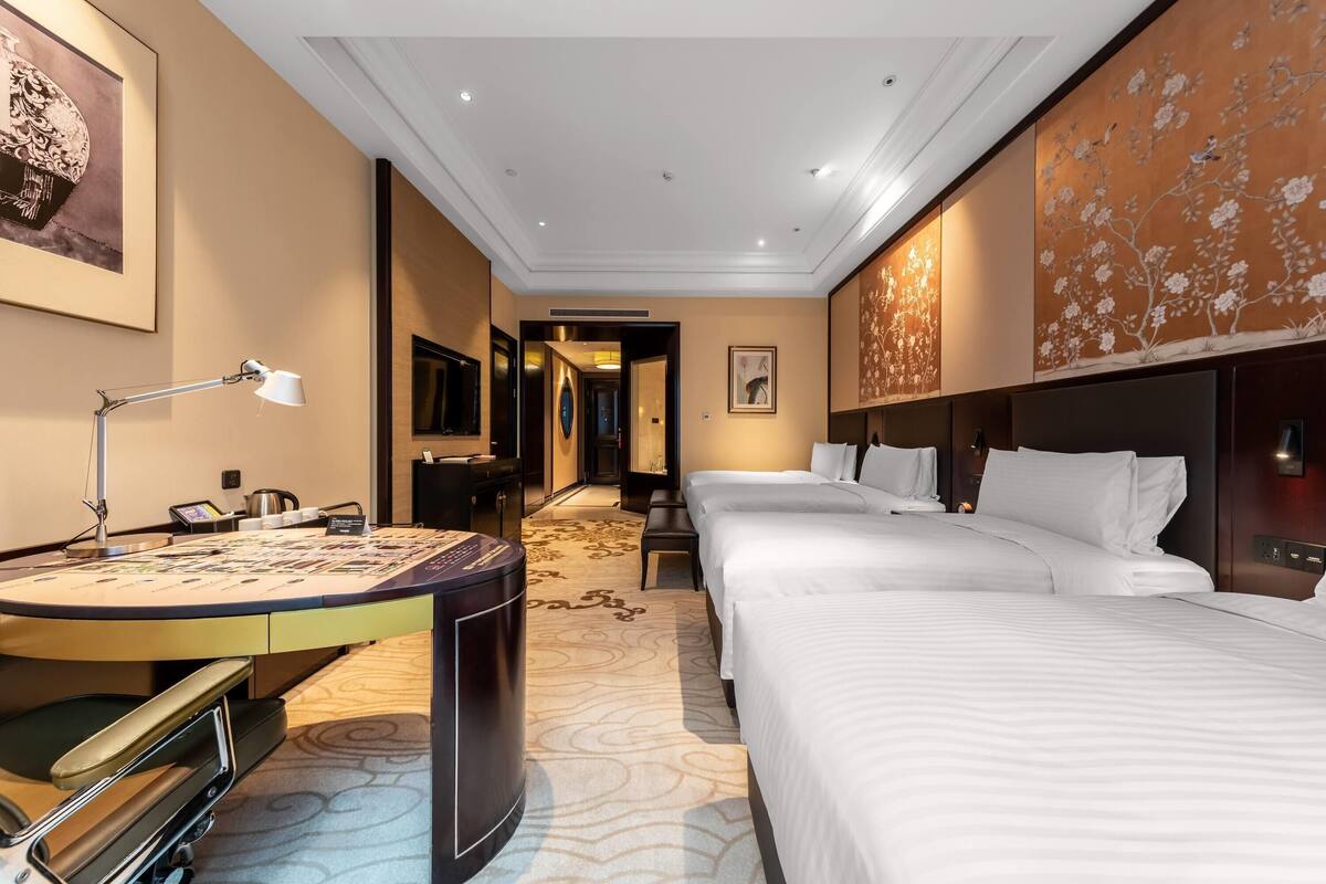 A hotel room with a desk, two beds, a TV, and a large floral wall mural.