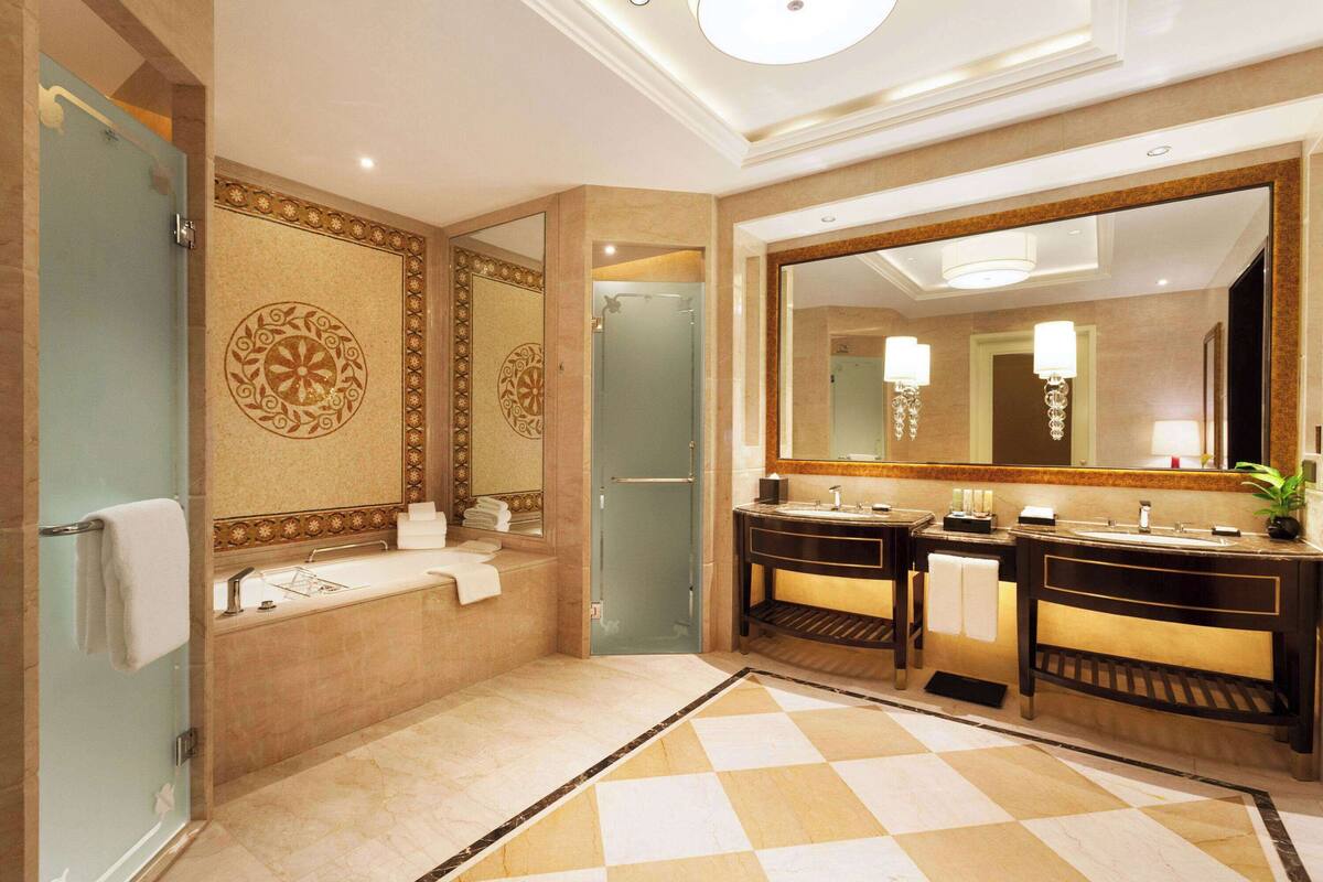 A luxurious bathroom with a large mirror, two sinks, a bathtub, and decorative tiles.