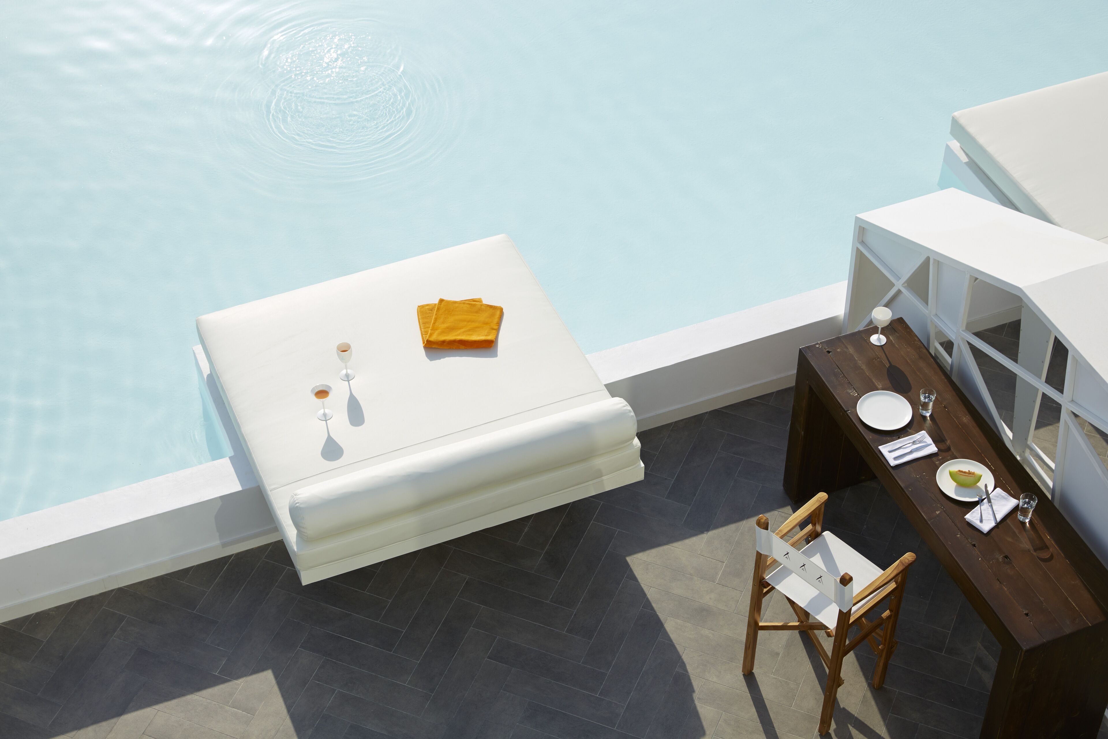 Un área junto a la piscina con un sofá blanco, una mesa de madera con una silla y un comedor.