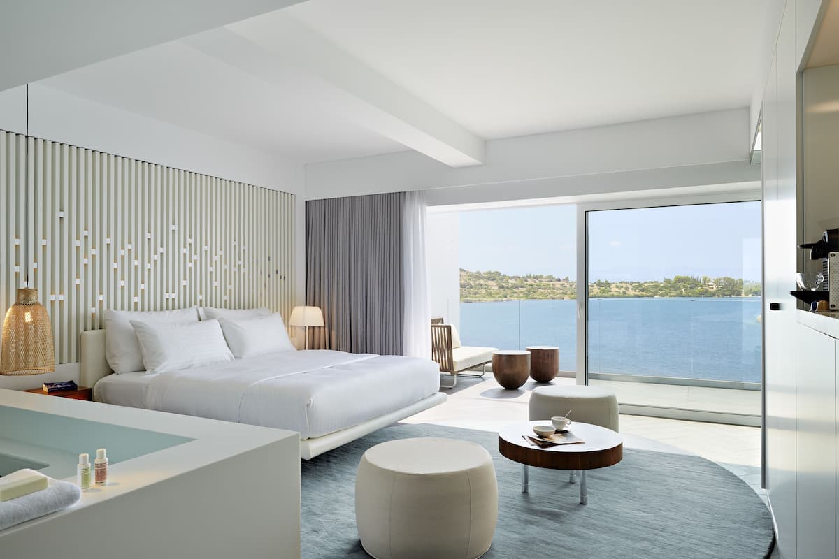 Ein modernes Hotelzimmer mit einem großen Bett, einer Sitzecke mit Tisch und Meerblick.