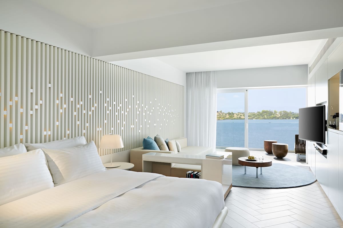 Ein modernes Hotelzimmer mit einem großen Bett, einer Couch, einem Schreibtisch und einem Fernseher. Das Zimmer verfügt über ein großes Fenster mit Meerblick.