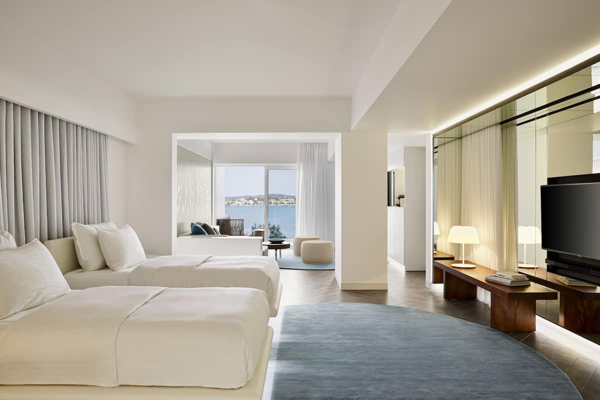 Ein modernes Hotelzimmer mit zwei Betten, einem großen Fernseher und Blick auf die Stadt.