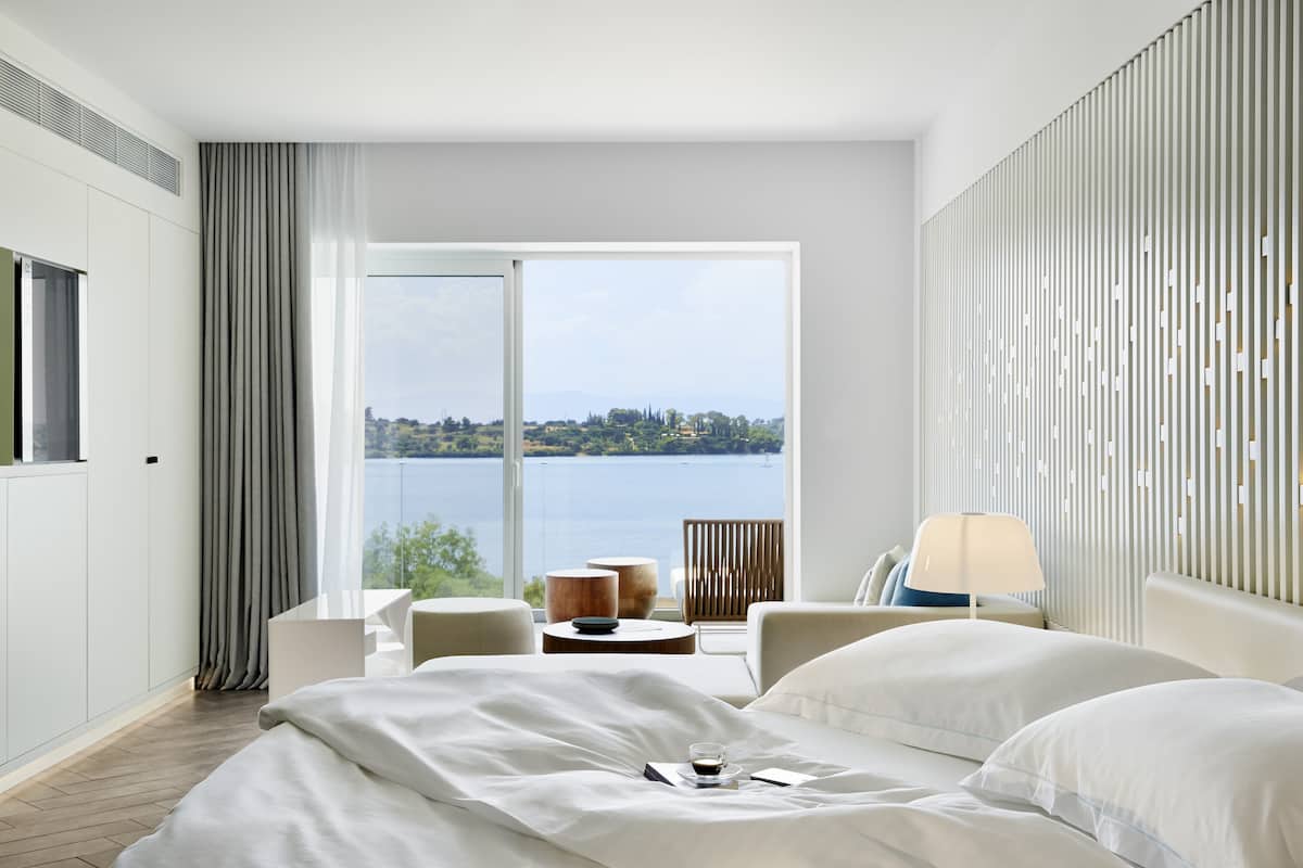 Ein modernes Hotelzimmer mit einem großen Bett, Seeblick und einem Balkon mit Tisch und Stühlen.