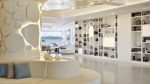A modern interior with a white sofa, a large bookshelf, and a view of the sea. - Nikki Beach Resort & Spa Porto Heli (Ermionida)