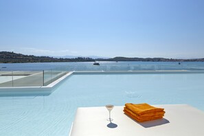 A poolside area with a clear view of the water, a glass of drink, and a stack of towels. - Aliis Resort Porto Heli (Ermionida)