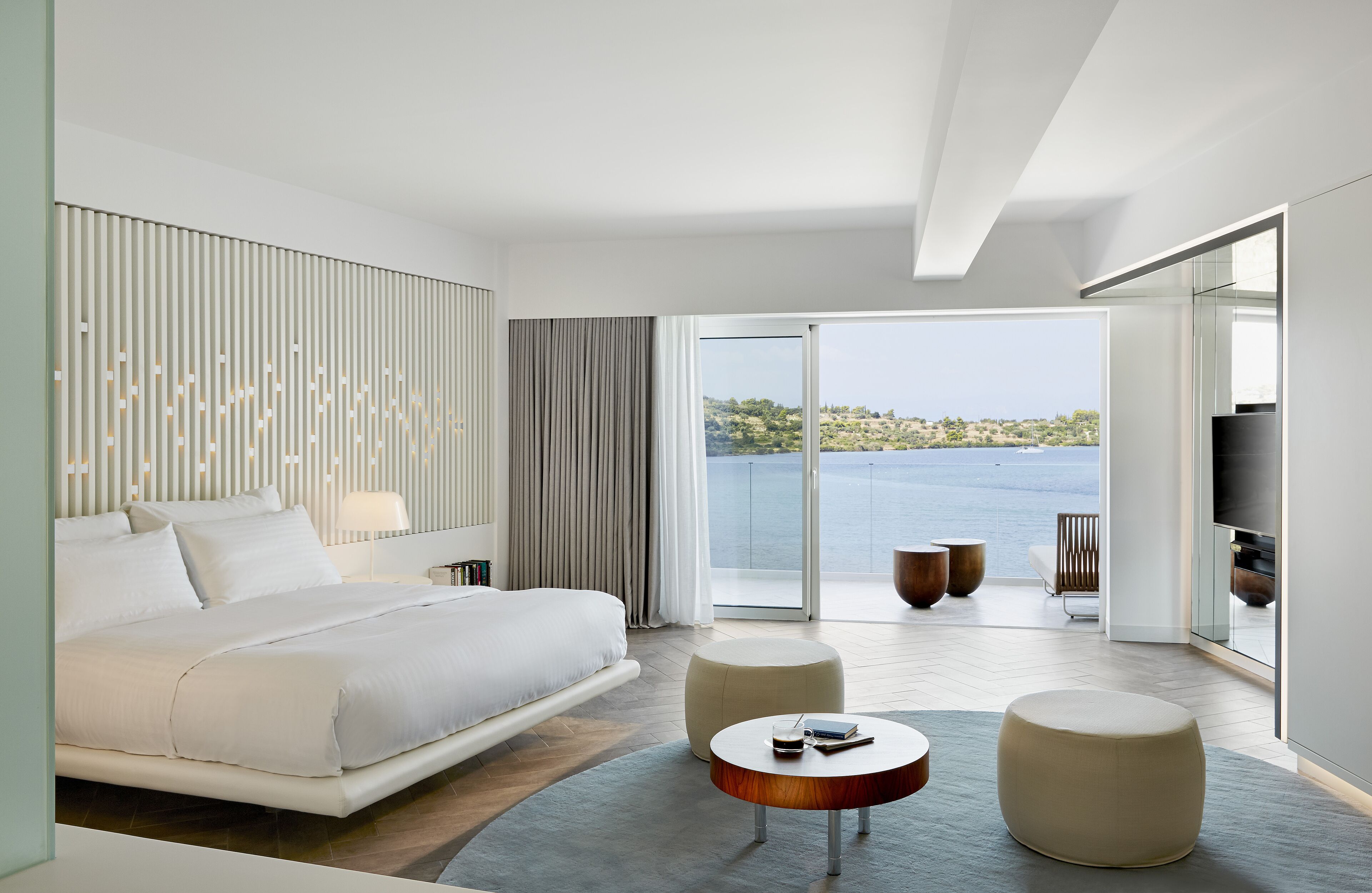 A modern hotel room with a large bed, a balcony with a view of the sea, and a flat-screen TV.